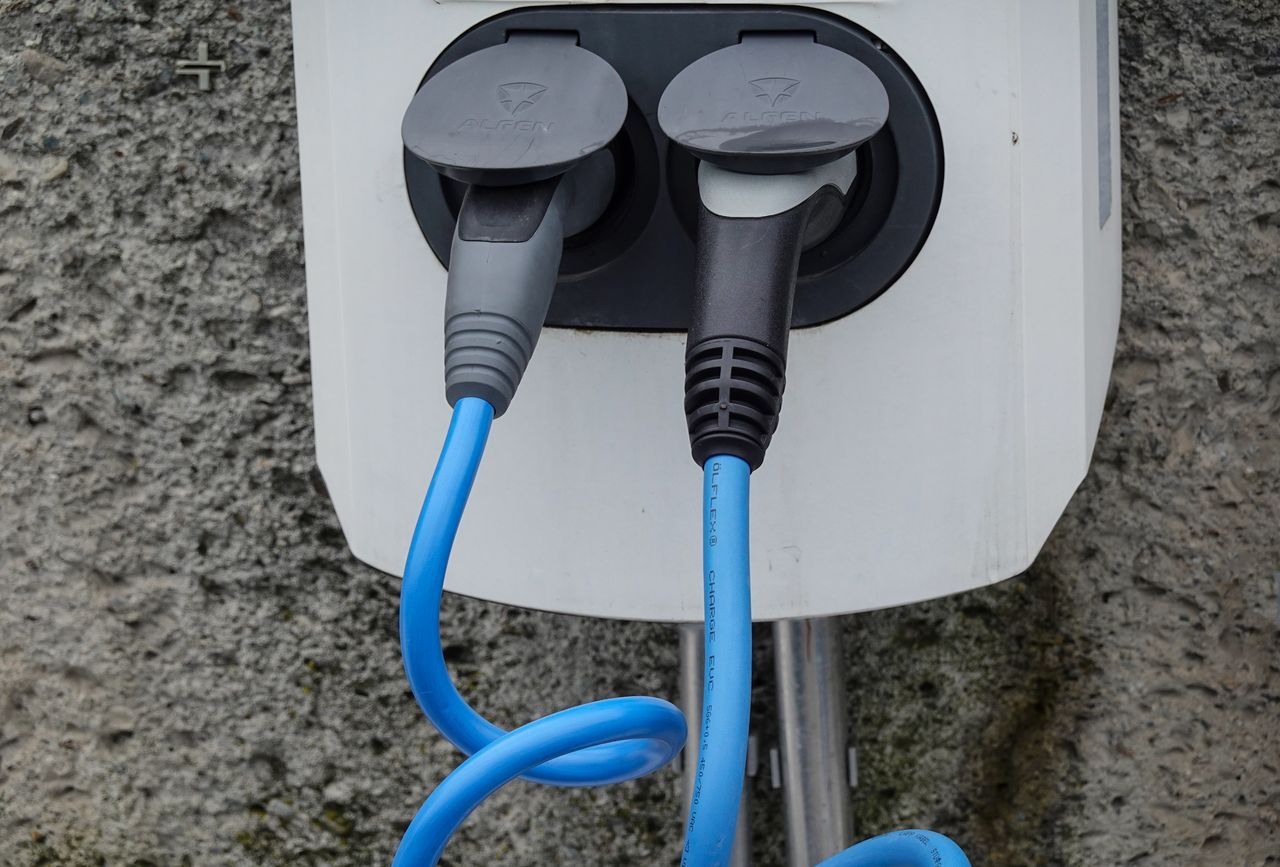 Close-up of an electric vehicle charging station with two cables in sockets against a textured wall.